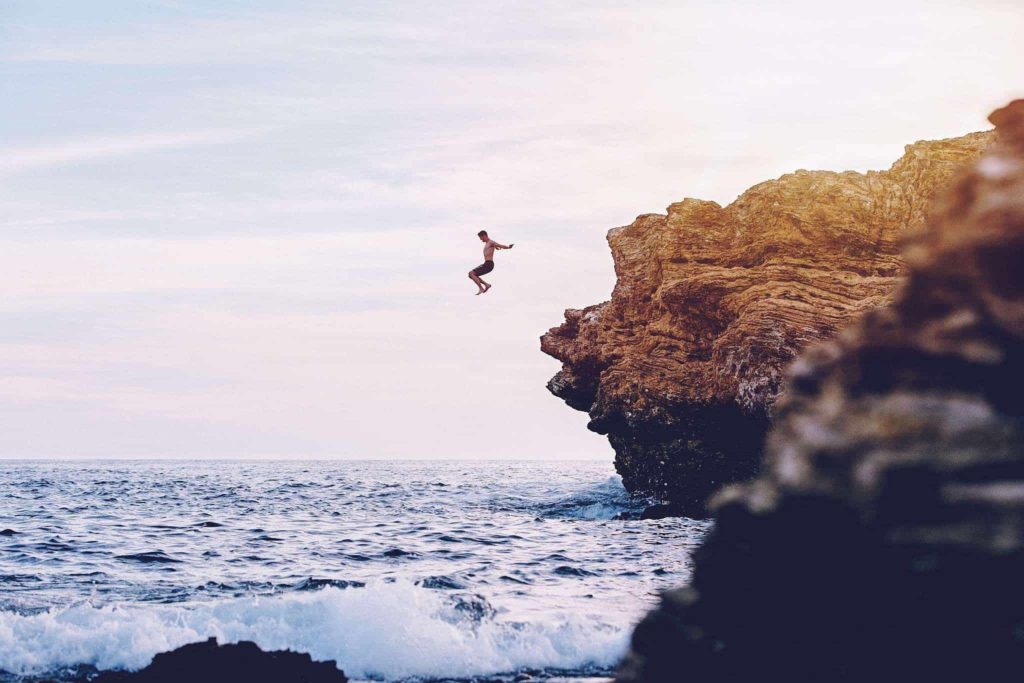 young man jumping off of a rock into the sea